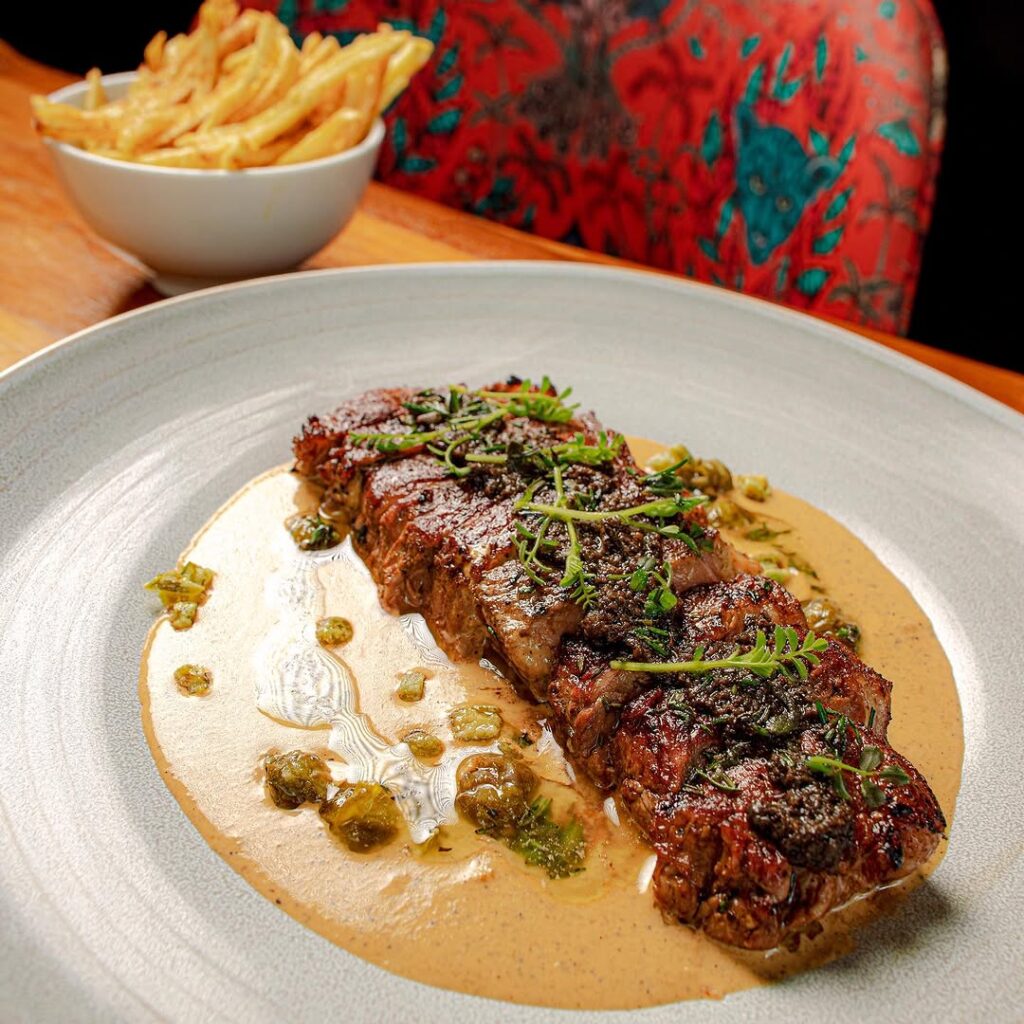 Pepper steak surrounded by a glazed stew and garnished with green herbs.