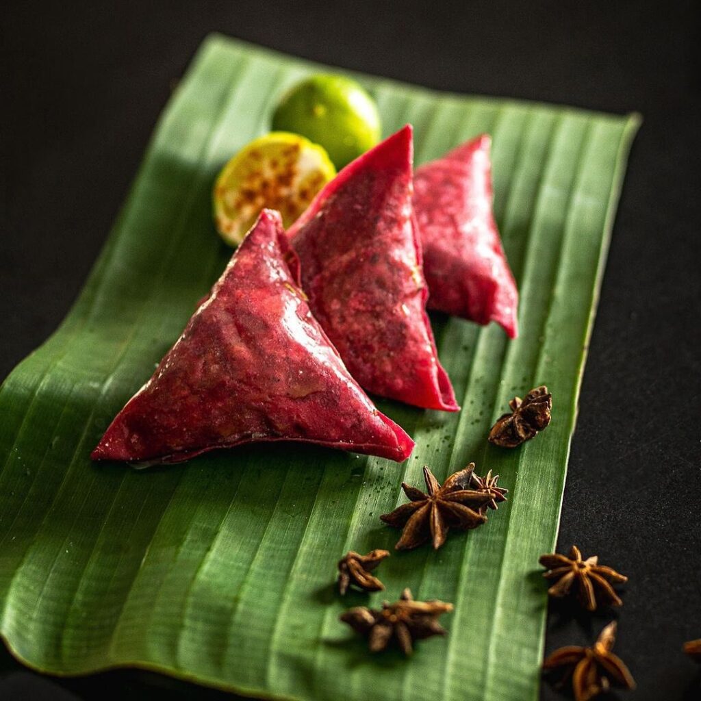 Pink samosas served on a banana lead with a citrus fruit and star anise.