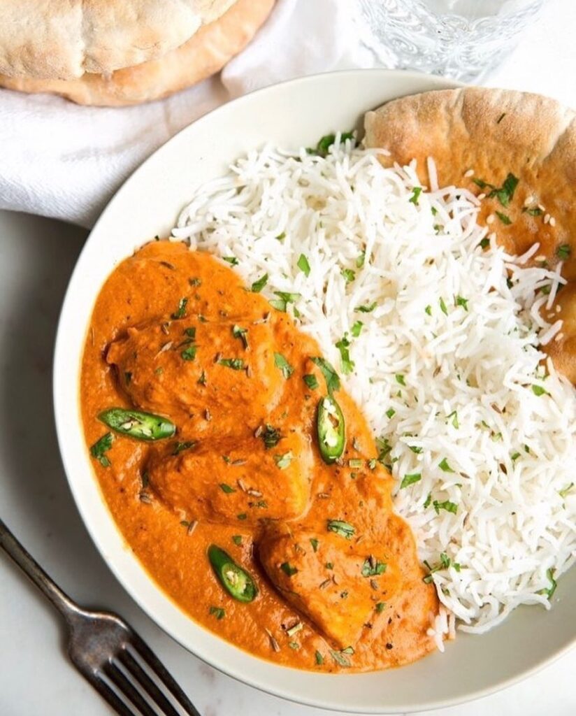 Orange chicken curry garnished with three slices of chilli served with rice and roti on a white plate in one of the best Indian restaurants in Nairobi.